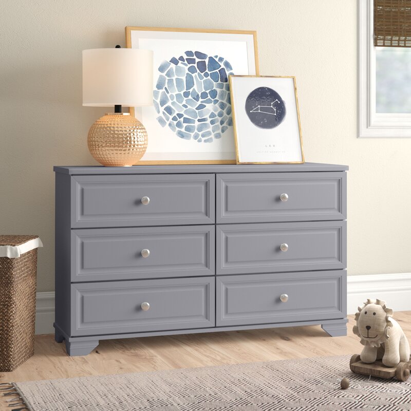 Wooden dresser against a wall with lap and picture frame on top.
